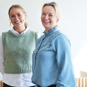 Två kvinnor som är glada och tittar in i kameran