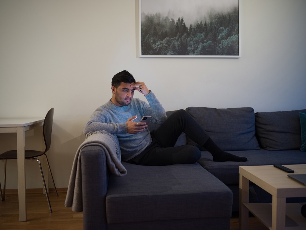 En man som sitter i soffan och scrollar på sin mobil