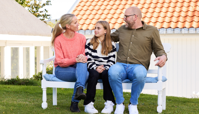 En mamma, pappa och barn sitter på en bänk och pratar