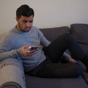 Man som sitter i soffan och tittar på sin mobil