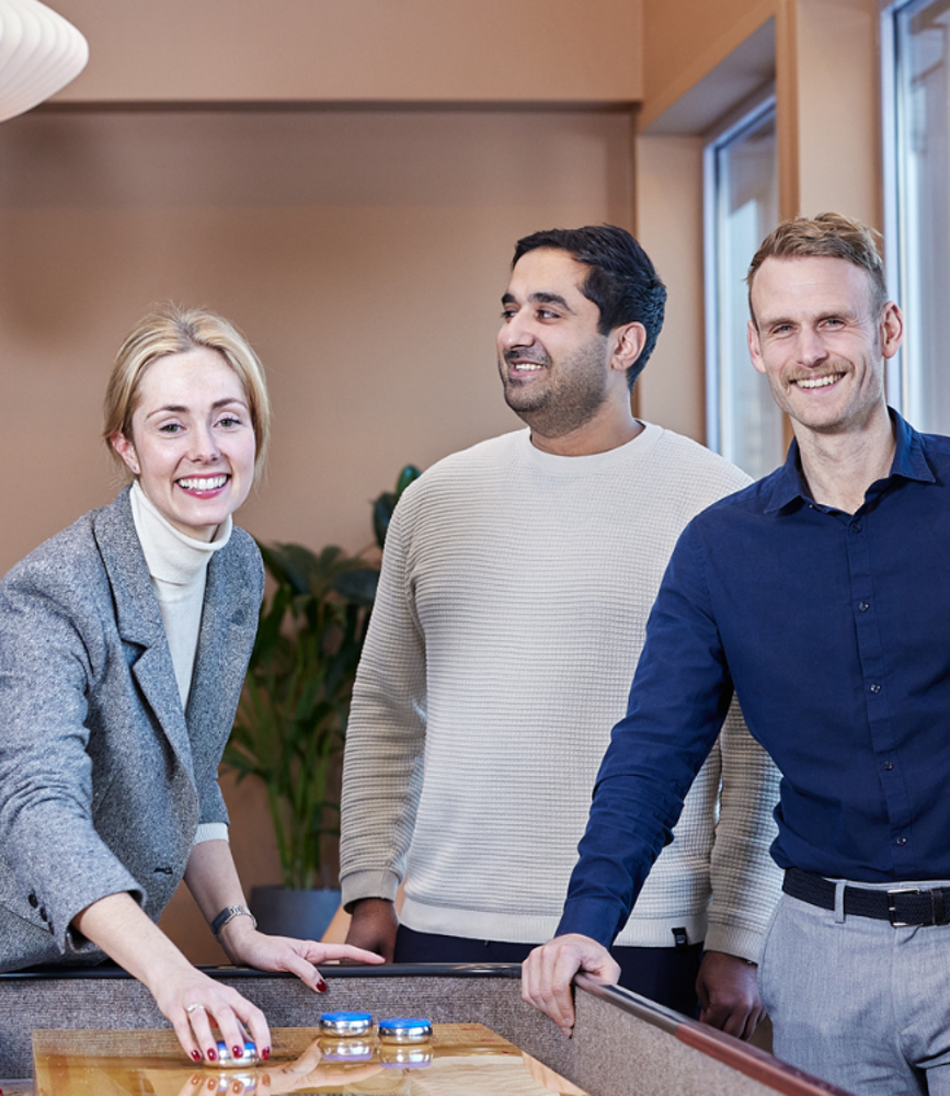 En kvinna och två män som står vid ett shuffleboard